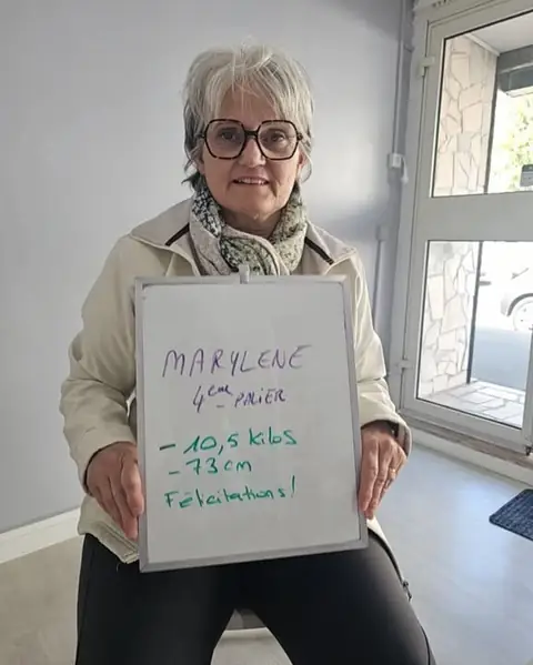 Une membre du club sourit et désigne le bilan qu’elle a inscrit à l’ardoise